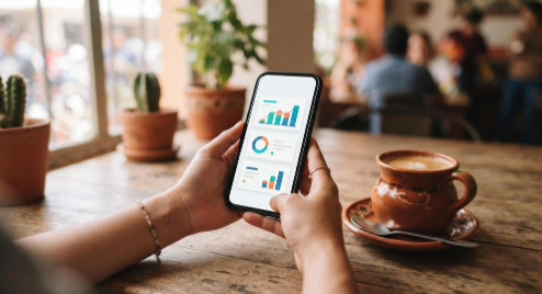 Cómo funciona un crédito digital sin ir a sucursal: del registro a tu cuenta en minutos 2 Manos sosteniendo un teléfono celular mostrando una interfaz de banca móvil moderna y limpia, con un café al lado sobre una mesa de madera